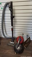 Full view of Dyson canister vacuum with hose, extension wand, and floor head on floor against wall