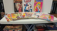 Overview of Femforce comics displayed on white table, front covers visible showing variety of comic issues with colorful artwork and characters.