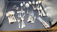 Full view of assorted flatware pieces arranged on black surface including forks, knives, spoons, and serving utensils.