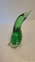 Green glass penguin figurine with bubble inclusions, side view showing body curve and clear base.