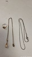 three items displayed: ring at left, pearl pendant necklace center, silver chain necklace right