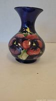Front view of Moorcroft vase with red and purple pansy flowers on deep blue background