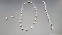 Full view of pearl necklace, crystal bracelet, and pearl earrings arranged on a gray surface.