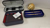 Wide shot of the Tommy Hilfiger wallet in original box, set of Parker pens in blue case, and signed lacrosse ball.