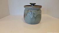 Front view of blue toned ceramic pot with lid, showing drip glaze pattern and lid knob