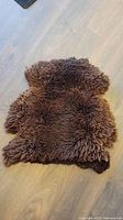 Top view of the large brown sheepskin showing thick, curly wool texture, laid out on a wooden floor.