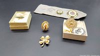 Four leaf clover brooch with pearls, assorted petite point brooches including oval and round floral designs, a rectangular scarf clip with floral needlepoint, and a decorative round gold-tone brooch with floral detailing and black and white floral button.