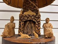 Close up image showing carved wood figures of a man, woman, cat and dog positioned in front of a carved fireplace on the lamp base.