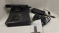 Xbox 360 console with controller, Kinect sensor, power brick, and manual laid out on a white surface in a corner.