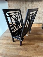 Black metal magazine holder with Art Deco geometric patterns, placed on a wooden surface against a tiled wall.