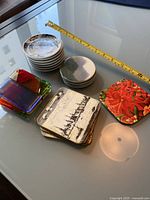 Photo showing various coaster sets laid out on a glass surface with a measuring tape for scale.