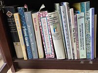 Photo of 13 assorted cookbooks arranged upright on a shelf showing titles and partial author names