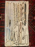 Overview of assorted necklaces on white cloth showing a wide range of styles and materials including beads and chains.