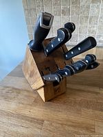 Henckels kitchen knife set in wooden block angled to show knives and sharpener clearly on a wooden countertop with tiled backsplash.