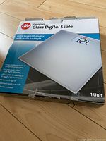 Photo of Life Designer Glass Digital Scale box showing front with product image and features including extra large LCD display with backlight, tempered safety glass, 150kg max weighing capacity, measures in kg or lb, automatic on/off and batteries included.