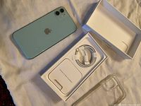 Green iPhone 11 back with dual camera, original open box with charging cable, and clear acrylic case