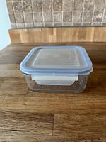 Small rectangular glass storage container with secure blue lid on wooden surface
