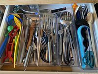 Drawer with assorted kitchen utensils including peelers, graters, spatulas, tongs, kitchen shears, ladles, measuring spoons, and other small tools