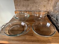 Top-down view of clear glass kitchenware on wooden counter, showing two bowls and two round dishes.