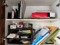 Cabinet shelf with notebooks, folders, papers, and desk organizer with small office supplies.