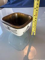 Photo showing the square pottery bowl with a tape measure indicating approximately 10 cm height, showing insect illustrations on the exterior and brown glazed interior.