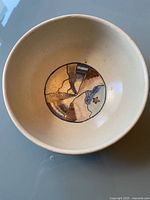 Top-down view of ceramic pottery bowl showing interior abstract painted design in brown, blue, and beige earth tones.