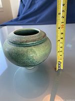 Photo of a small round green glazed pottery bowl/vase with measuring tape showing height around 4 inches.