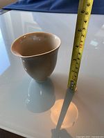 Photo of pottery vase with measuring tape showing height approx 7cm. Vase is off-white with slight spout lip on one side.