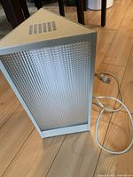 Triangular white light therapy lamp with textured translucent front panel, power cord coiled on floor.