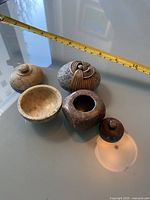 Image showing four small art pieces: three carved containers with lids and one wrapped stone art piece with woven fiber.