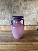 Purple-toned glass vase with dark handles on wood surface with tiled background