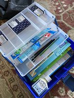 Open view of the plastic case showing watercolour palette, brushes, paper pad, ink bottle, and other supplies.