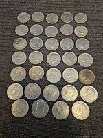 Top-down view of 34 US half dollar coins arranged on dark fabric surface. Coins show varied wear and some tarnish, mainly Kennedy design.