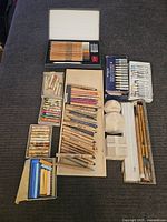 Full view of artist supplies showing pastel sticks, pencils, brushes, and blending tools spread out and organized in boxes and trays