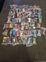 Top view of about 50 diecast toy cars in individual bags, placed on a dark surface