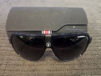 Photo showing black Carrera sunglasses placed in front of the black hard carrying case with Carrera embossed logo.