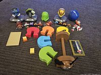 Photo showing an assortment of Five Nights at Freddy's figures, colorful plastic letter pieces, and small collectible items spread on a carpet.
