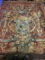 Full view of vintage tapestry depicting ornate heraldic shield, cherubs, fruits, and floral elements on a red background.