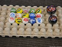 Photo showing 14 advertising shooter marbles with various soda brand logos including Pepsi, Coca-Cola, Sprite, Grapette, and Marble Collector. Marbles are colorful with vintage style logos and some years printed.