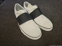 Pair of white Puma slip-on shoes angled front-right view on dark fabric background.