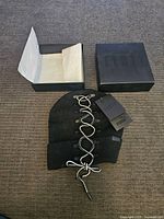 Black knit beanie with white and black lace-up front detail, Puma Fenty tags attached, displayed next to black Puma box and paper wrapping.