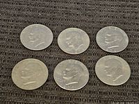 Six US Eisenhower $1 coins arranged on fabric surface showing obverse side with President Eisenhower profile.