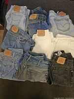 Lot of eight folded Levi's jeans in assorted colors and denim washes shown from front with leather patches visible.