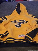 Front view of yellow vintage hoodie with black sleeves detailing and hood lining, showing U.S. Polo Assn. 3 embroidered on the chest and patch detail on pocket.
