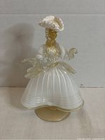 Front view of white and gold blown glass lady figurine with wide skirt and hat