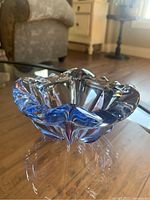 Image showing heavy vintage glass ashtray with blue and purple accents on glass surface, placed on a glass table.