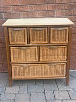 Front view of wooden cabinet with five wicker basket drawers, natural wood frame, and sanded top.