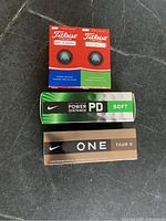 Photo showing 4 Titleist DT golf balls and 2 boxes of Nike golf balls (Power Distance Soft and One Tour D).