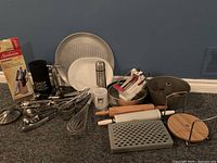 Overview photo showing the entire kitchen lot with baking pans, cutting utensils, and kitchen tools spread on the floor against a blue wall.