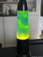 Lava lamp lit showing yellow lava blobs floating in green liquid inside a black base and top.